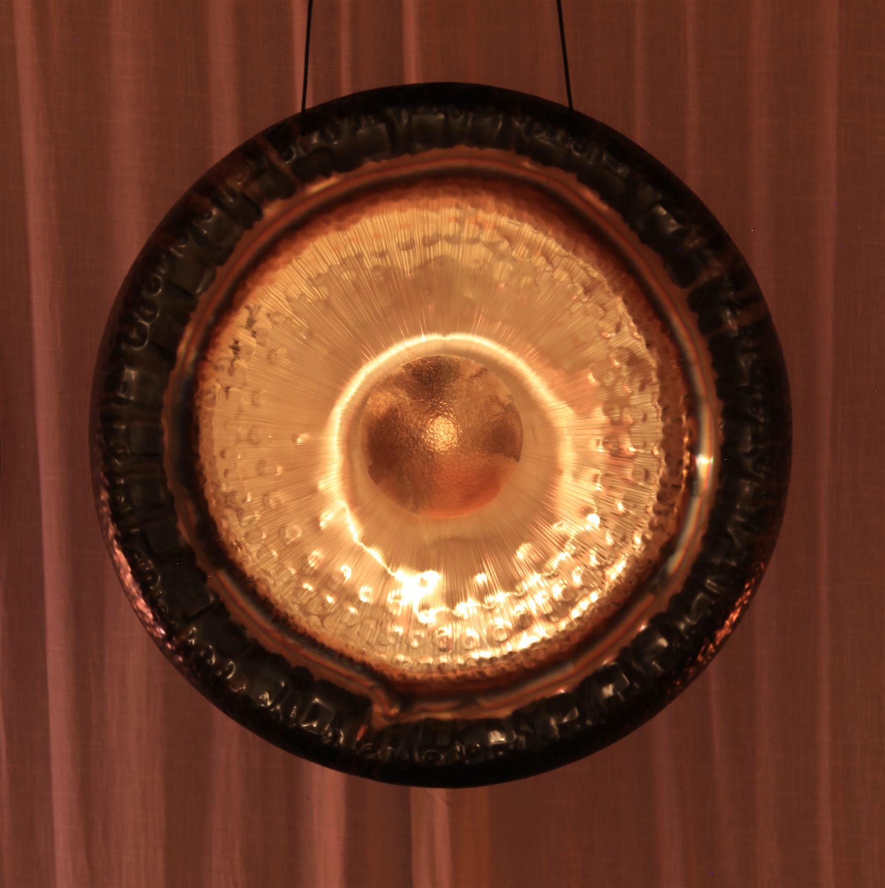 Nahaufnahme eines Gongs, von hinten warm beleuchtet, das Zentrum glüht golden.