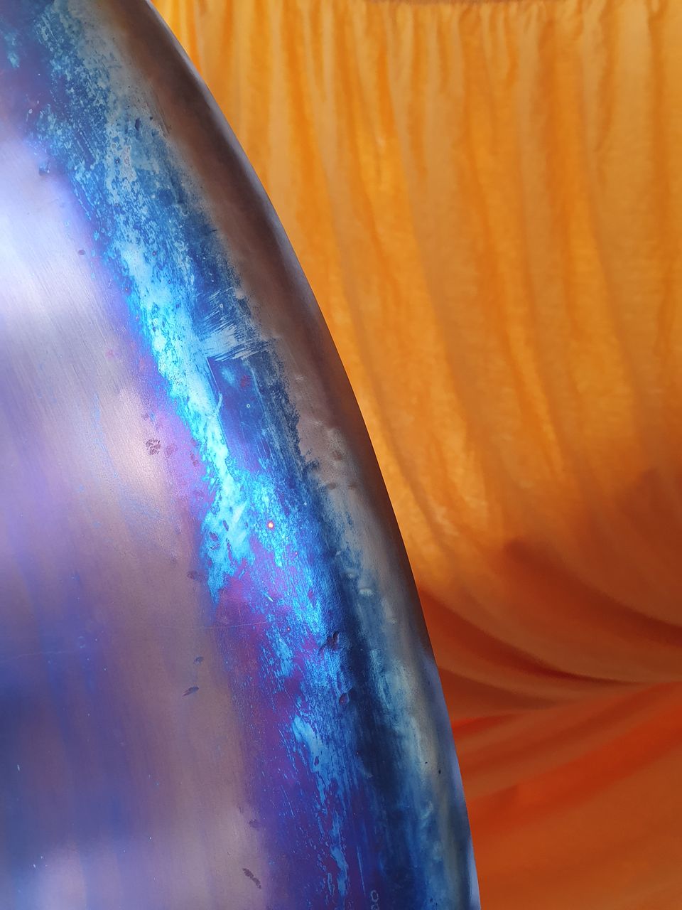 Nahaufnahme eines Gongs: Der Rand schimmert in Blau und Violett vor einem orangefarbenen Tuch.
